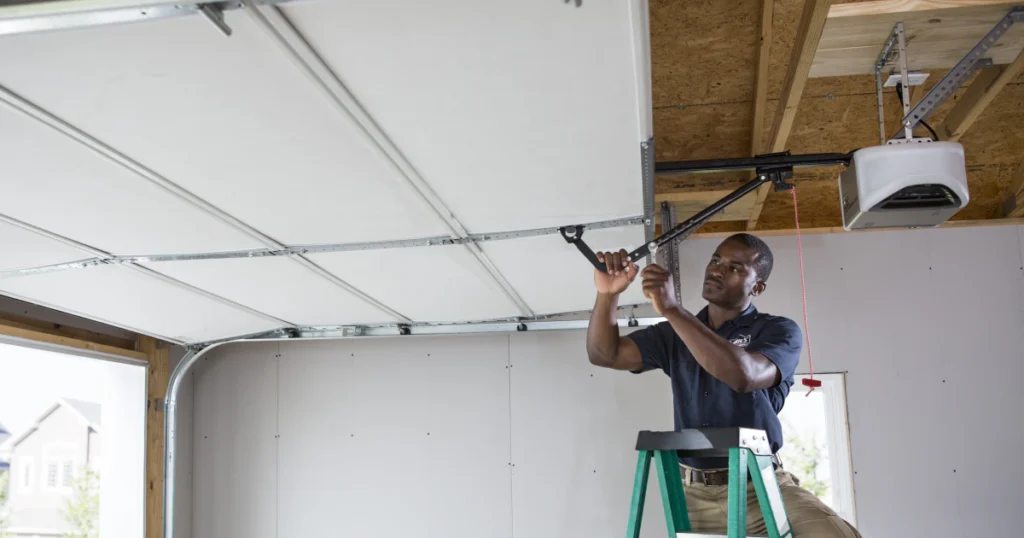 Person working on a garage door mechanism while on a ladder.