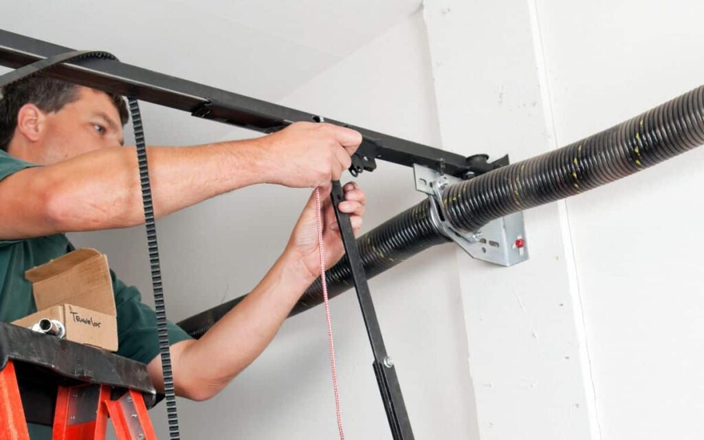 Man repairing a garage door opener on a ladder.